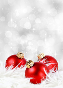 Christmas background with red ornaments on feathers against a festive sparkling silver background