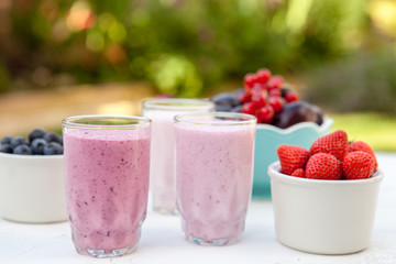 Three small glasses of smoothie on the white table in the garden