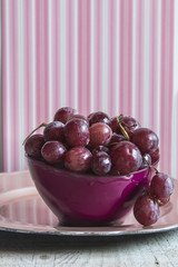 Fresh red grapes in a purple bowl over wooden background. Rustic