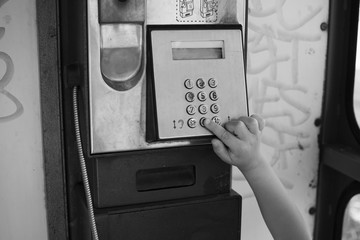 Child in a phone booth, dialing a number. Black and white photo.
