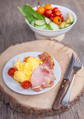 Breakfast: scrambled egg and bacon with salads, vegetables on a dark wooden table, selective focus