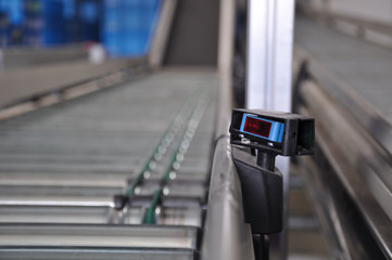 Close up shot of a roller conveyor with a laser distance sensor on the side. Photo taken in a big...