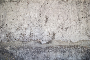 Weathered, aged and cracked gray stone wall with names scratched on it.