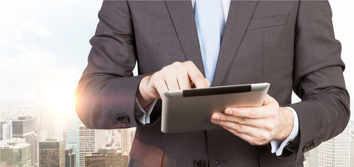 A man in formal suit is looking for some data in the tablet. Panorama of New York city on the...