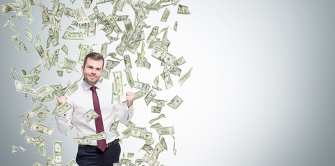 Happy successful manager or businessman is getting benefits from his job. Dollar note are falling down from the ceiling. Concrete background.