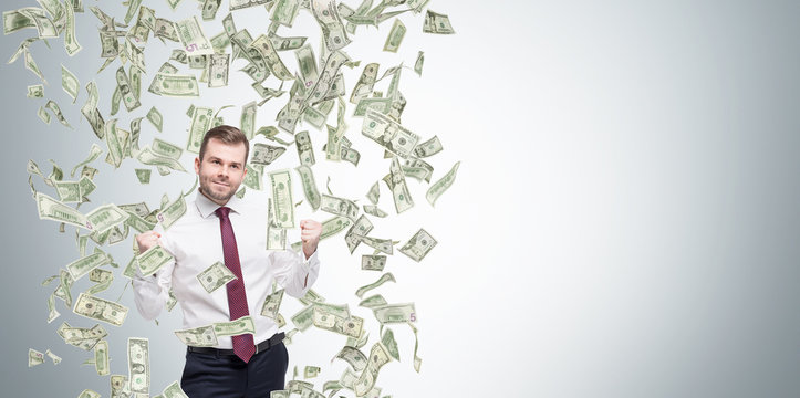 Happy successful manager or businessman is getting benefits from his job. Dollar note are falling down from the ceiling. Concrete background.