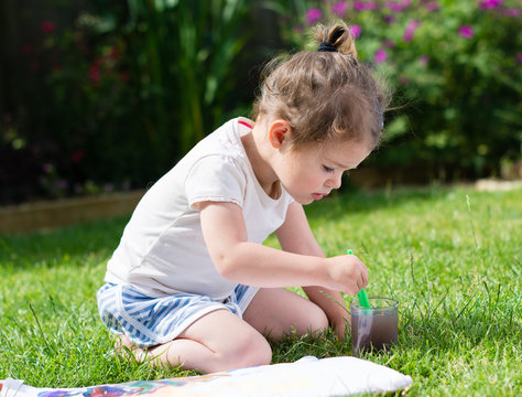 Little toddler girl painting in the garden
