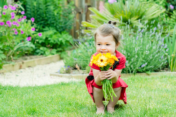 Toddler girl holding bright orange flowers in the garden