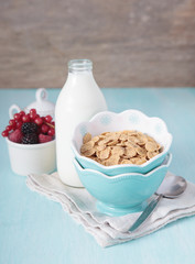 Cereals in the blue bowl with milk and fruit on the background