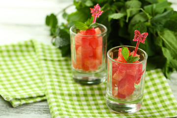 Cold watermelon pieces in glasses, on wooden table background