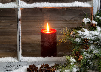 Christmas red candle with snow covered home window and pine tree