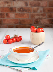 Tomato soup with tomatoes on the background on the white table, brick wall background