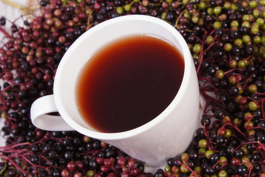 Cup of hot tea with elderberry juice and heap of berry, healthy nutrition