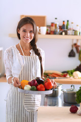 Smiling young woman holding vegetables standing in kitchen