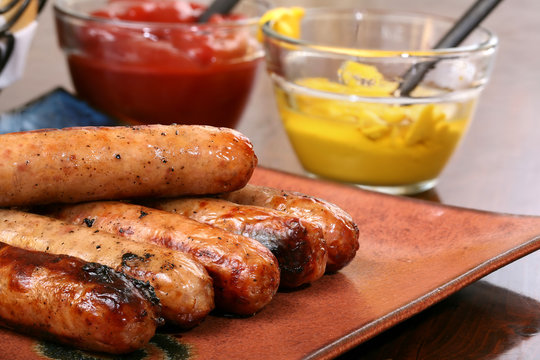 Grilled brats stacked on a plate ready to serve with condiments ketchup and mustard and buns