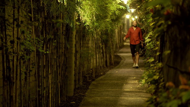 Young man walking through narrow bamboo path at night