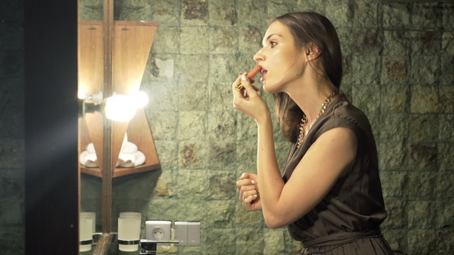 Pretty, elegant woman applying lipstick in bathroom at night
