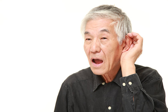senior Japanese man with hand behind ear listening closely