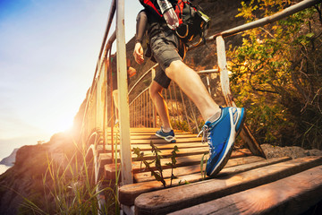 Man hiking in mountains, walking on wooden bridge at sunset. Healthy lifestyle.