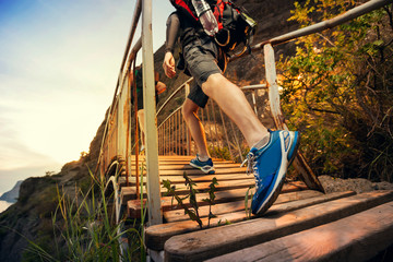 Man hiking in mountains, walking on wooden bridge at sunset. Healthy lifestyle.