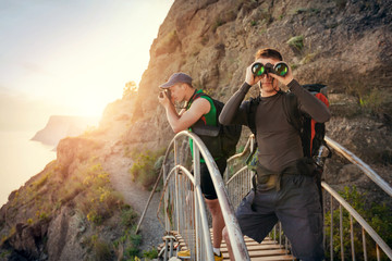 Men with camera traveling in the mountains. Guys stand on the bridge and looking through binoculars and photograph nature.