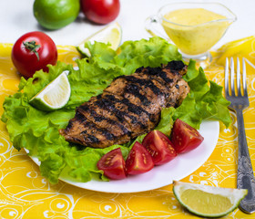 Fresh grilled chicken fillet with with lettuce, tomatoes and limes. Dish is in white wooden table on yellow cloth with fork. Ceasar sauce served together with dish.