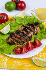 Fresh grilled chicken fillet with with lettuce, tomatoes and limes. Dish is in white wooden table on yellow cloth with fork. Ceasar sauce served together with dish.