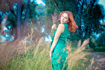 Obraz na płótnie Canvas Romantic red-haired young woman in green long dress Walking