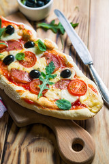 Homemade pizza with salami, black olives and fresh arugula