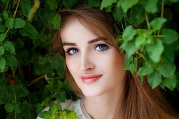 Happy smiling beautiful young woman surrounded by green leaves