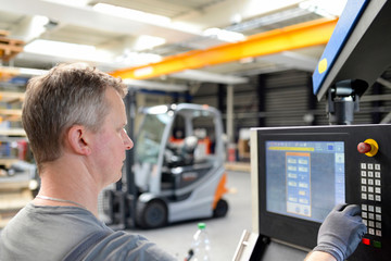 Arbeiter in der Industrie bedient eine Maschine, im Hintergrund Interieur der Fabrikhalle //...