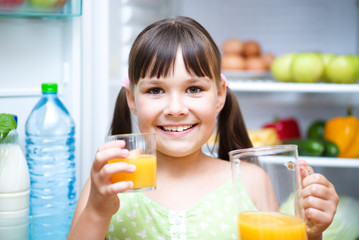 Girl drink orange juice standing near refrigerator