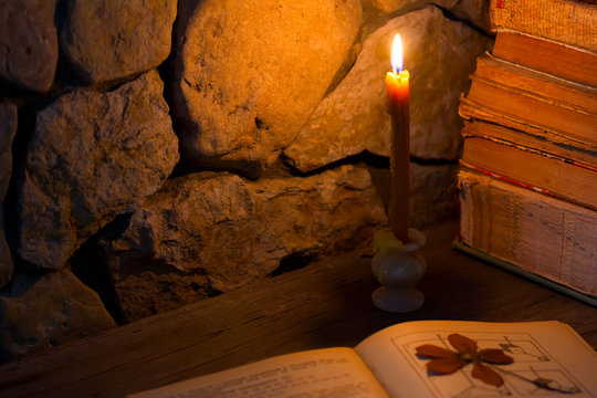 near a stone wall lit candle on the table and lie old books, selective focus