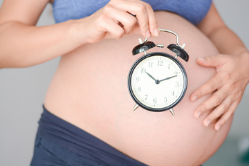 Pregnant woman holding clock suggesting time to arrive