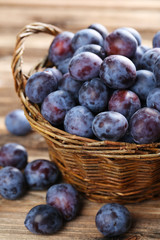 Fresh plums in basket on the brown wooden background