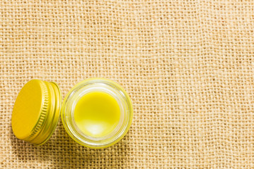 herbal balm in glass pot on gunny bag texture, top view with copy space