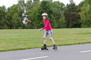 Smiling little girl roller skating in a public park on a beautiful spring day. The girl has a...