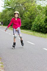 Obraz premium Smiling little girl roller skating in a public park. The girl has a helmet and protective knee and wrist pads
