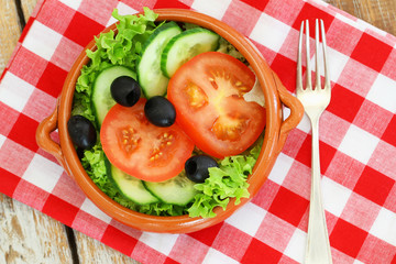 Salad with lettuce, tomatoes, cucumber and black olives in clay bowl
