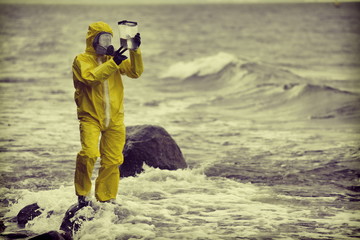 Specialist in protective suit checking sample of water in container on rocky sea, ocean shore