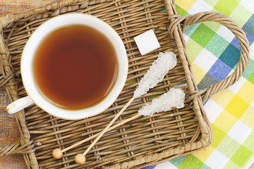 Black tea in porcelain cup and white sugar on wicker tray
