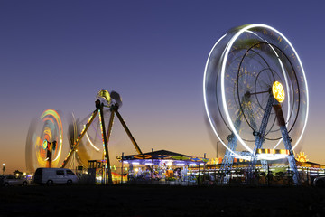 Colorful carnival Ferris wheel and gondola spinning in motion blurred at twilight in an amusement...