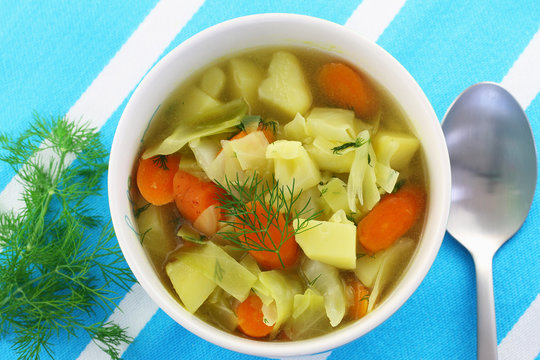 Cabbage soup garnished with fresh dill in bowl on checkered cloth
