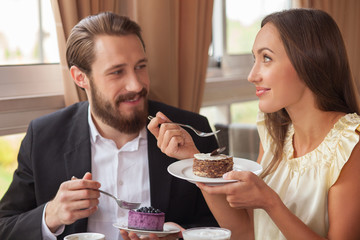 Attractive man and woman are tasting sweet food in cafe