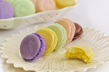 Colourful colorful sweet macarons tasty cookies biscuits dessert food. Confection flavors include  cassis, chocolate, citron, pistachio, raspberry, and lemon. Bite taken out of one yellow lemon one.