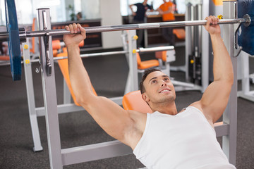 Cheerful young male sportsman is training in fitness center