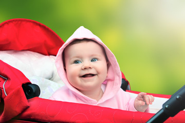 Smiling little baby girl sitting in the red pram on green background