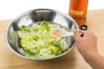Hand pouring spoonful of Apple Cider Vinegar to soak and remove pesticides residue from vegetable