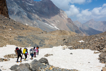 Group of Hikers Walking on Snowfield Alpine Climbers Team Sport Clothing with Heavy Backpacks and Climbing Gear Crossing Snow Place Mountain Landscape Blue Sky Clouds on Background