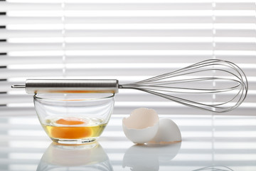 Whisk and glass bowl with broken egg
